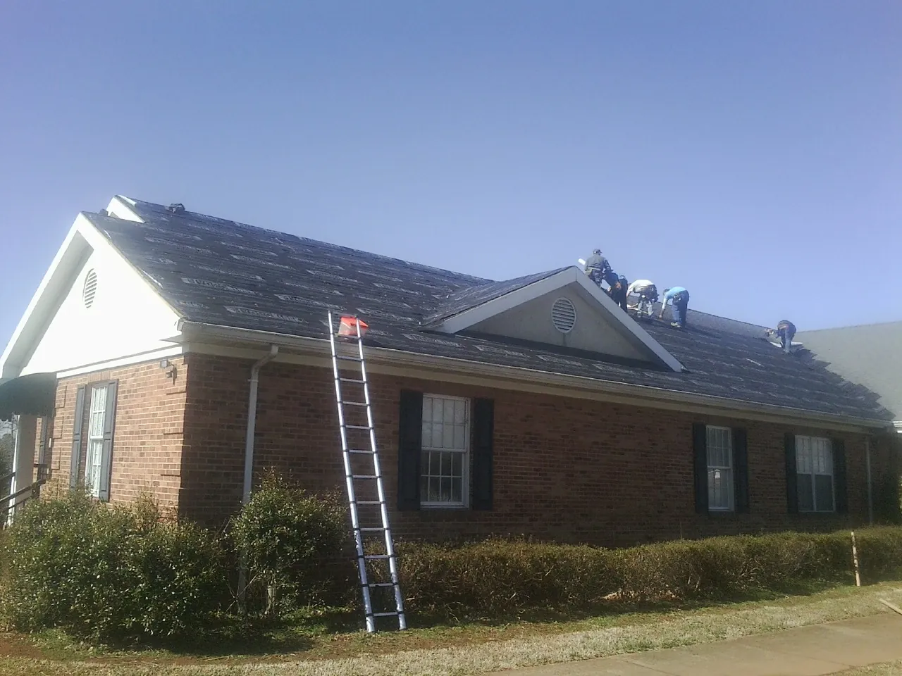 Crew tearing shingles off a brick ranch roof with a ladder set — Metal Roof Repair work by our crew in Ipswich