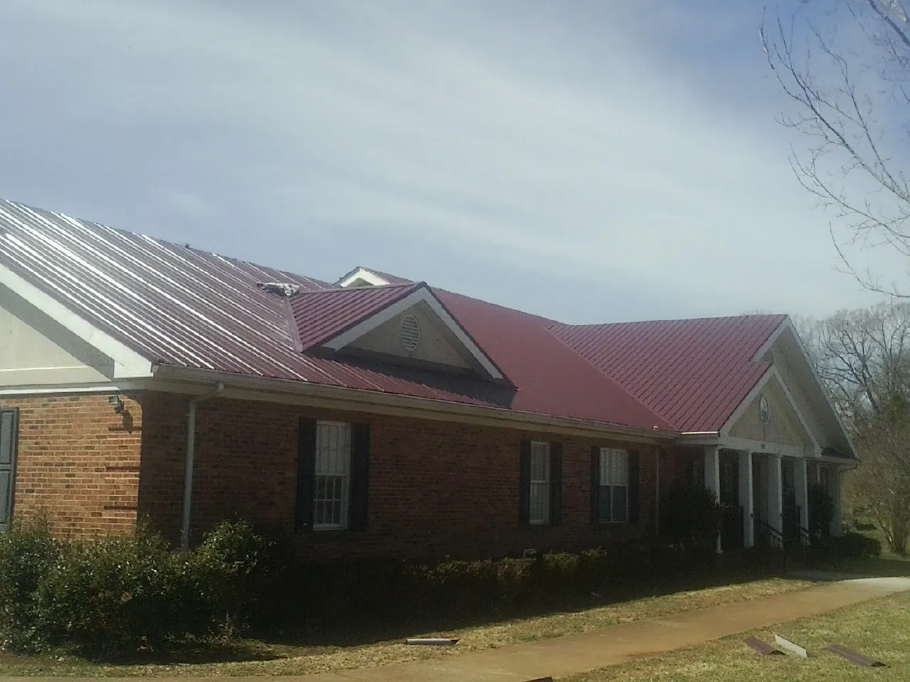 Red metal roof with gabled entries on a long brick building, from a Hail Damage Roof Repair job in Ipswich