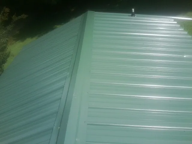 New green metal panels meeting at the ridge of a roof — Flat Roof Repair work by our crew in Ipswich