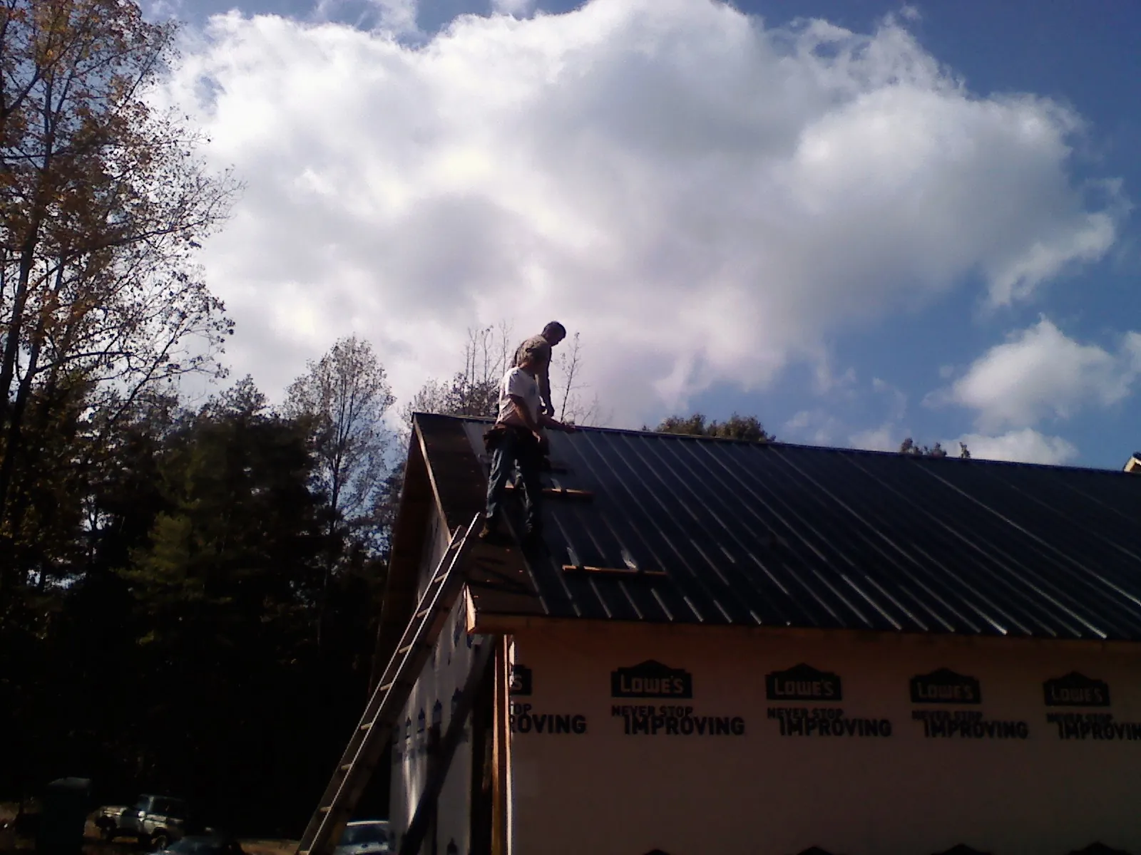 Roofer fastening dark metal panels high against a cloudy sky, from a Roof Inspection job in Ipswich